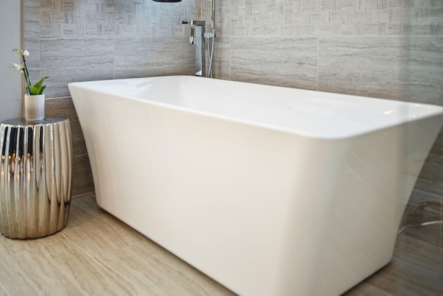 bathroom featuring a bath, hardwood / wood-style floors, and tile walls