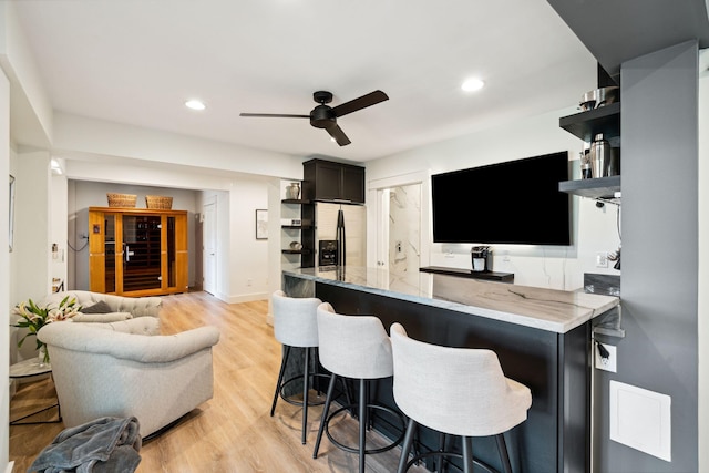 bar with ceiling fan, stainless steel fridge, light stone countertops, and light hardwood / wood-style floors