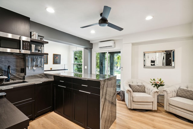 kitchen featuring sink, tasteful backsplash, kitchen peninsula, an AC wall unit, and light wood-type flooring