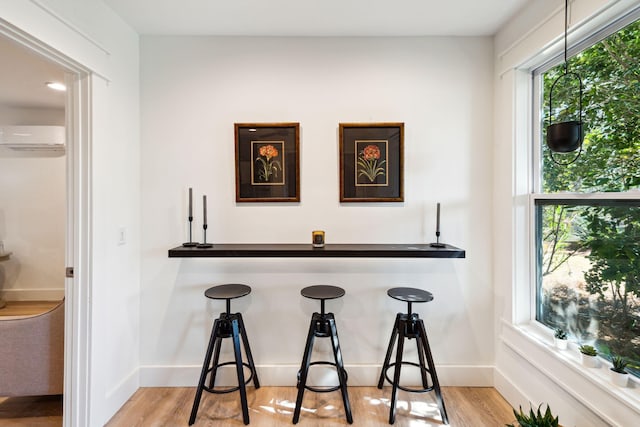 bar with a wall unit AC and light hardwood / wood-style flooring