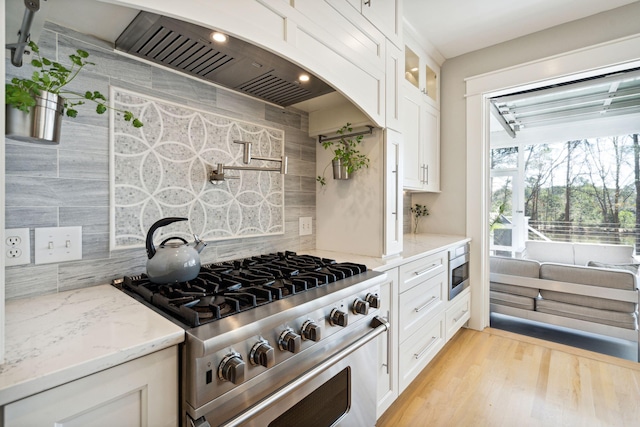 kitchen featuring appliances with stainless steel finishes, white cabinets, decorative backsplash, light stone countertops, and light wood-type flooring