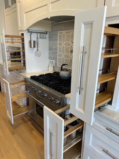 kitchen featuring white cabinetry, stainless steel range, backsplash, and light wood-type flooring