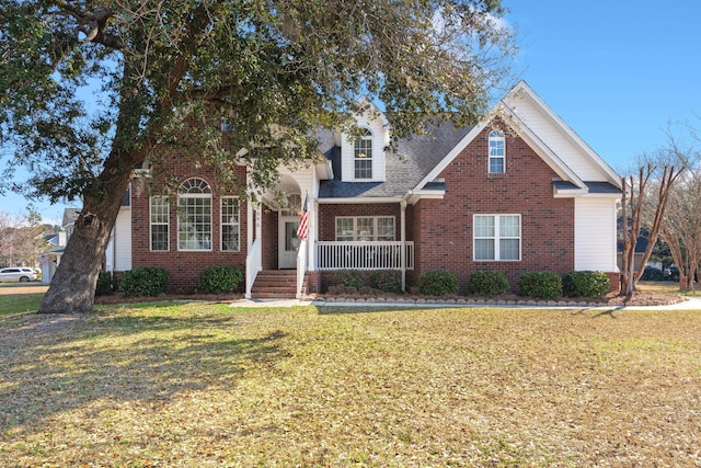 traditional home with covered porch, a shingled roof, a front lawn, and brick siding