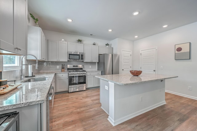 kitchen with sink, light stone counters, a center island, light wood-type flooring, and appliances with stainless steel finishes