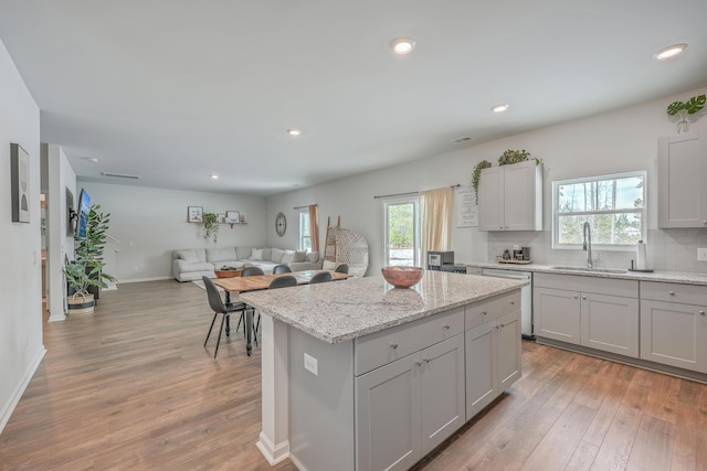 kitchen with sink, tasteful backsplash, light stone counters, light hardwood / wood-style floors, and a kitchen island