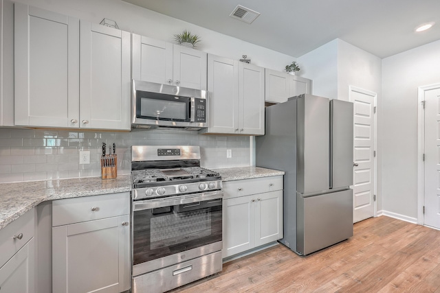 kitchen featuring light stone counters, decorative backsplash, stainless steel appliances, and light hardwood / wood-style floors