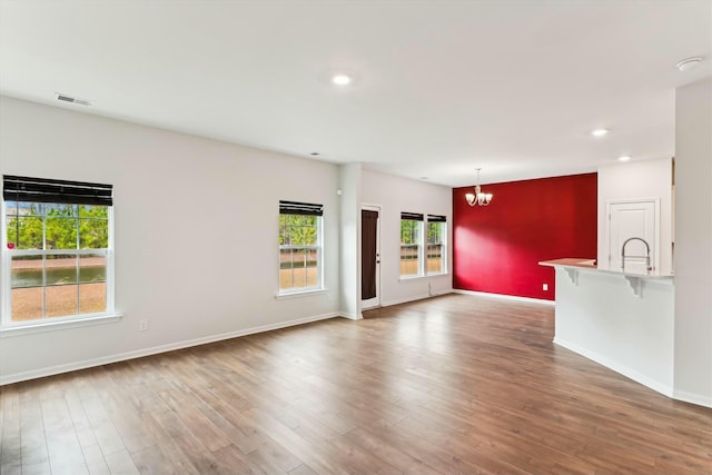 unfurnished living room with sink, a notable chandelier, and hardwood / wood-style flooring