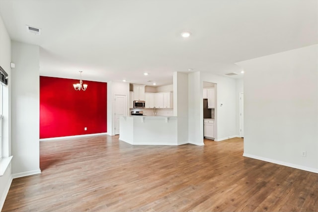 unfurnished living room featuring a chandelier and light hardwood / wood-style flooring