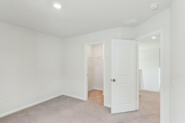 unfurnished bedroom featuring a walk in closet, a closet, and light colored carpet