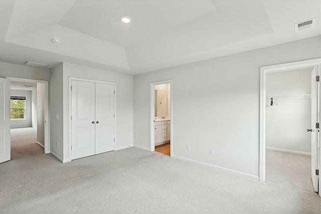 unfurnished bedroom featuring a tray ceiling, connected bathroom, light carpet, and a closet