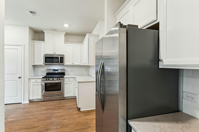 kitchen with tasteful backsplash, white cabinets, light wood-type flooring, and appliances with stainless steel finishes