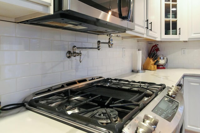 kitchen featuring tasteful backsplash, glass insert cabinets, appliances with stainless steel finishes, white cabinets, and light stone countertops