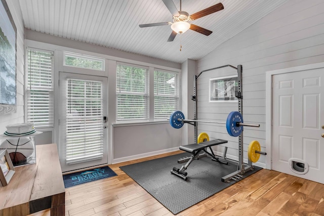 exercise room featuring wood walls, vaulted ceiling, hardwood / wood-style flooring, and ceiling fan