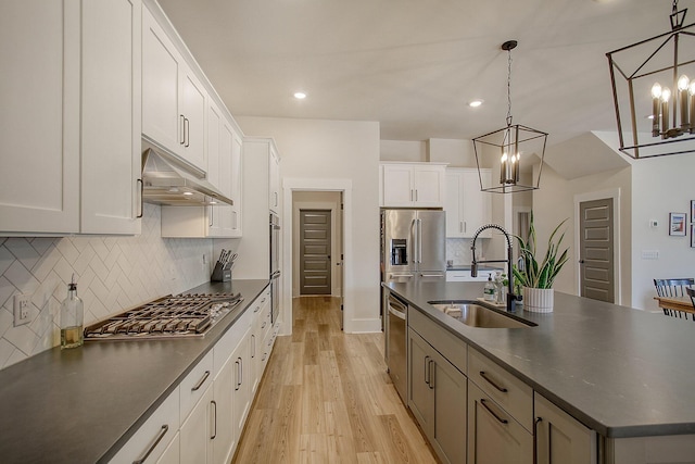 kitchen with dark countertops, stainless steel appliances, under cabinet range hood, and a sink