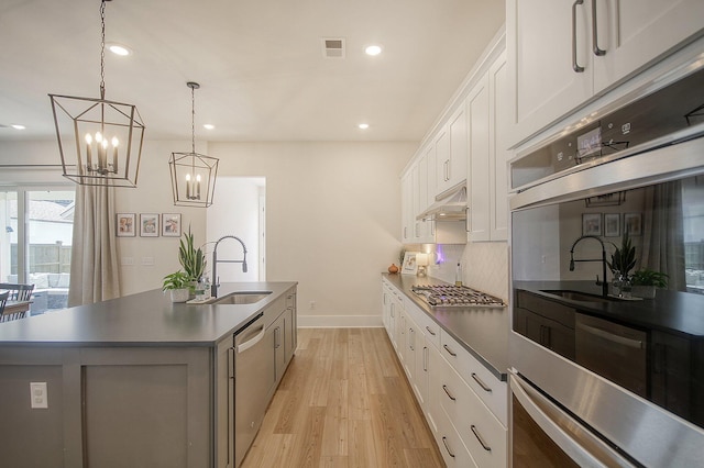 kitchen with dark countertops, under cabinet range hood, a center island with sink, appliances with stainless steel finishes, and a sink