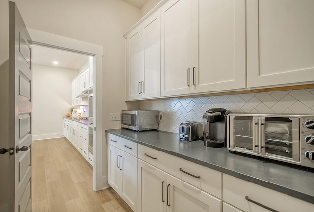 kitchen featuring stainless steel microwave, backsplash, light wood-style floors, white cabinets, and a toaster