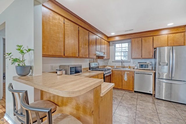 kitchen with kitchen peninsula, a kitchen breakfast bar, stainless steel appliances, sink, and light tile patterned flooring