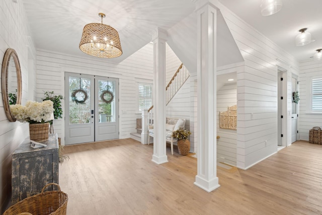 entrance foyer with decorative columns, wooden walls, an inviting chandelier, and light wood-type flooring