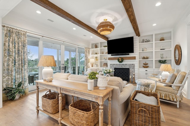 living room featuring beam ceiling, a brick fireplace, light hardwood / wood-style floors, and built in shelves