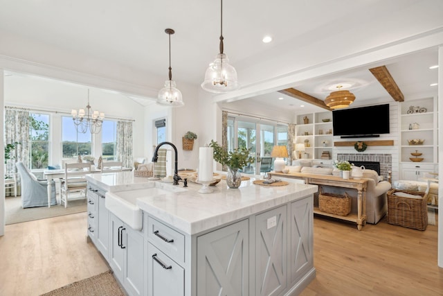 kitchen with sink, hanging light fixtures, light stone counters, a center island with sink, and a brick fireplace