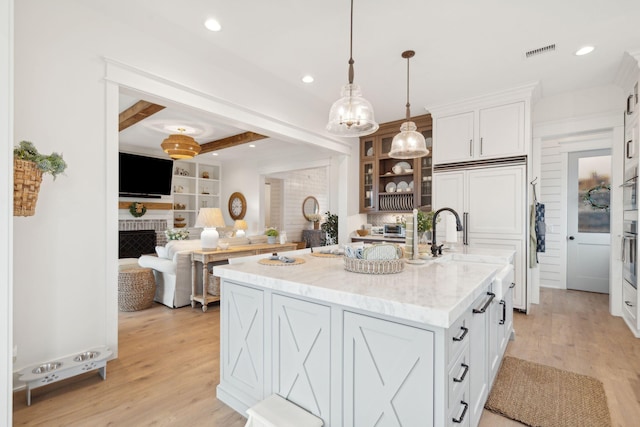 kitchen with white cabinetry, hanging light fixtures, light stone countertops, and a center island with sink