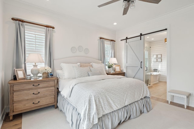 bedroom with connected bathroom, crown molding, light hardwood / wood-style flooring, ceiling fan, and a barn door