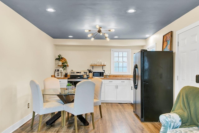 kitchen with light wood-type flooring, stainless steel electric range, freestanding refrigerator, an inviting chandelier, and white cabinets