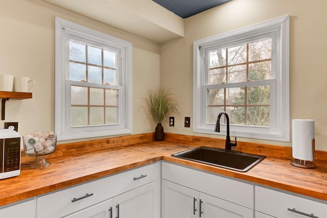 kitchen with a sink, butcher block countertops, and white cabinetry