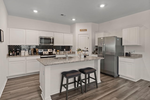 kitchen featuring white cabinets, appliances with stainless steel finishes, hardwood / wood-style flooring, and an island with sink