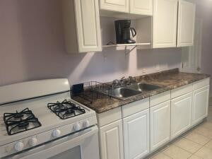 kitchen with dark stone counters, white cabinetry, sink, white stove, and light tile floors