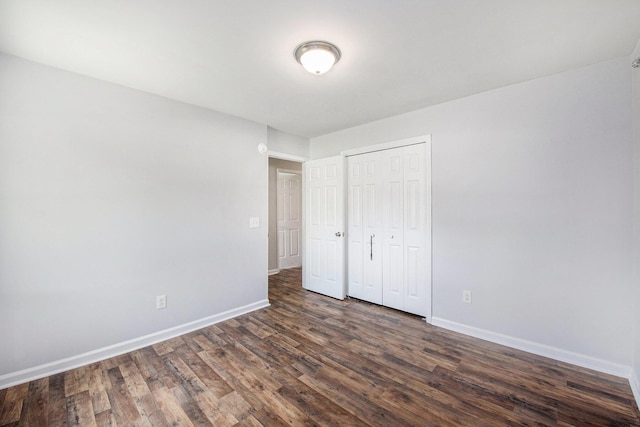 unfurnished bedroom with baseboards, dark wood-type flooring, and a closet