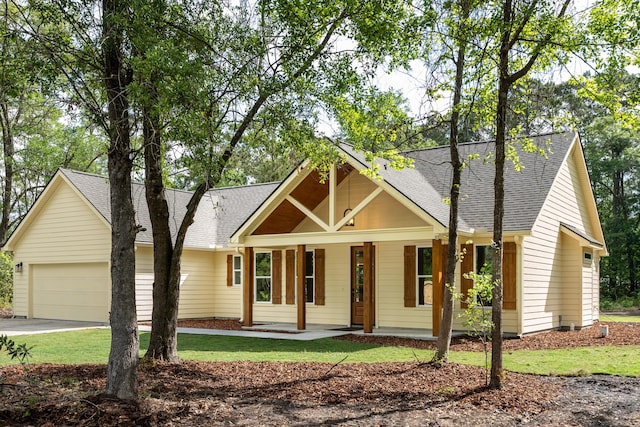 view of front facade with a porch, driveway, a shingled roof, and a garage