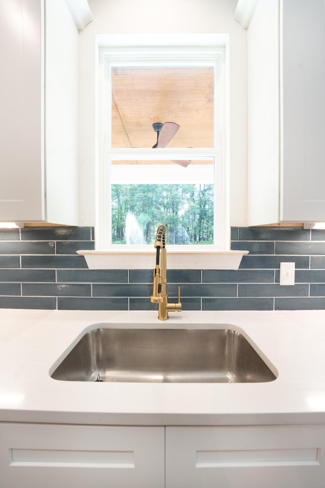 room details with a sink, light countertops, backsplash, and white cabinetry