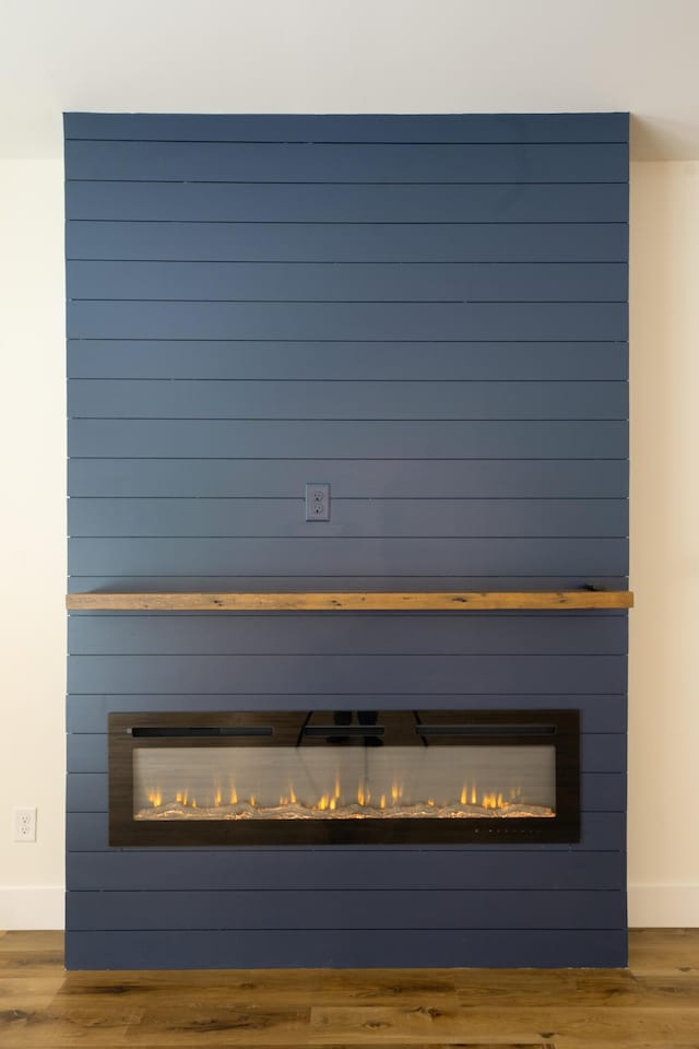 room details featuring a large fireplace, baseboards, and wood finished floors