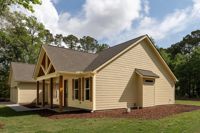 view of side of home with a lawn, covered porch, a shingled roof, and a garage