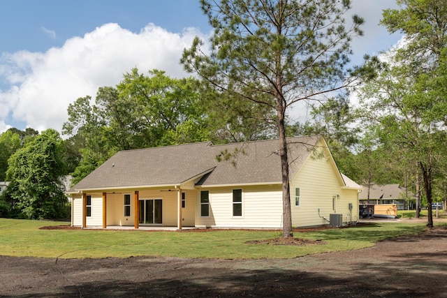 rear view of house featuring central AC unit, roof with shingles, and a yard