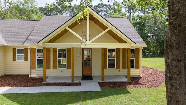 back of property with a porch, roof with shingles, and a yard