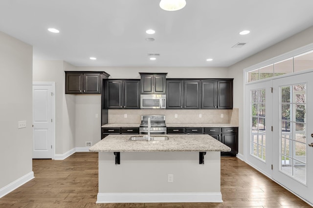 kitchen with wood-type flooring, stainless steel appliances, a breakfast bar, and a center island with sink