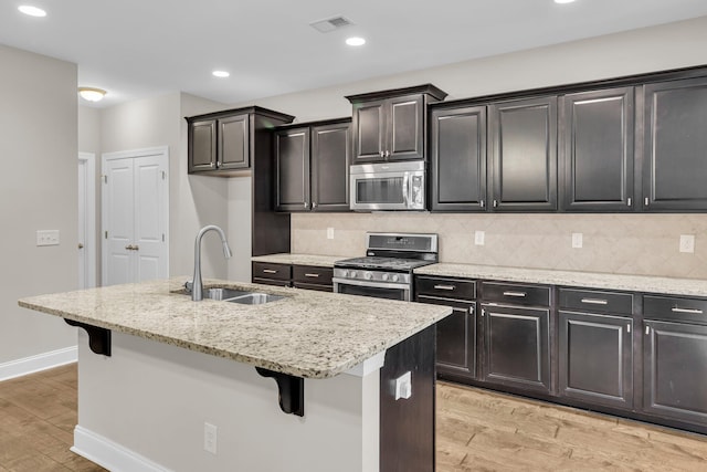 kitchen featuring sink, light hardwood / wood-style flooring, a breakfast bar, appliances with stainless steel finishes, and an island with sink