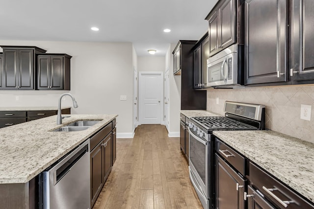 kitchen featuring sink, light hardwood / wood-style flooring, stainless steel appliances, light stone countertops, and decorative backsplash