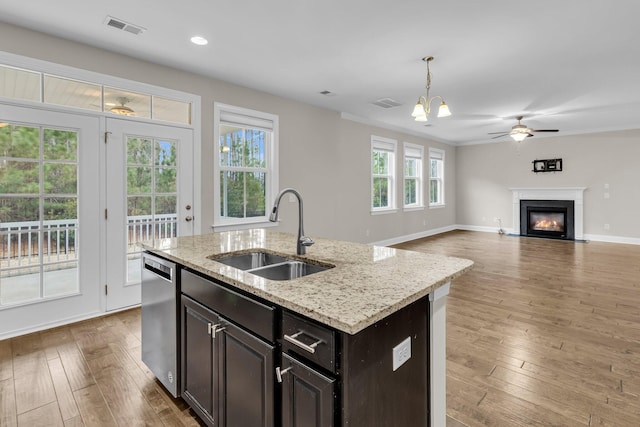 kitchen featuring sink, decorative light fixtures, a center island with sink, dishwasher, and light stone countertops