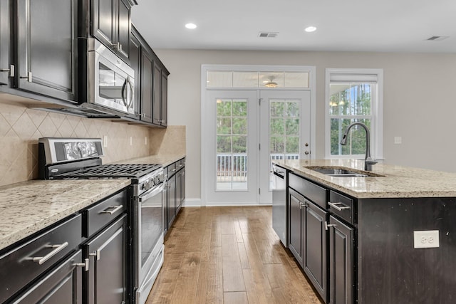 kitchen with appliances with stainless steel finishes, tasteful backsplash, sink, a kitchen island with sink, and light hardwood / wood-style floors