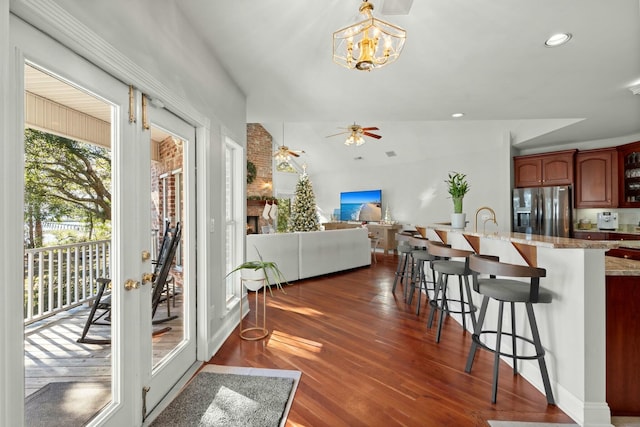 kitchen featuring stainless steel refrigerator with ice dispenser, dark hardwood / wood-style flooring, ceiling fan with notable chandelier, decorative light fixtures, and a breakfast bar area