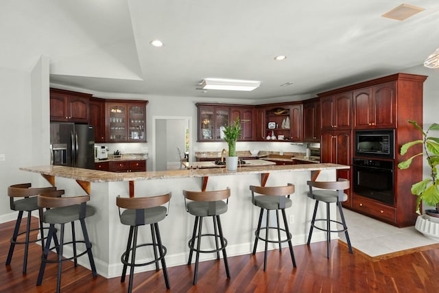 kitchen featuring a breakfast bar, light stone countertops, light hardwood / wood-style flooring, and black appliances