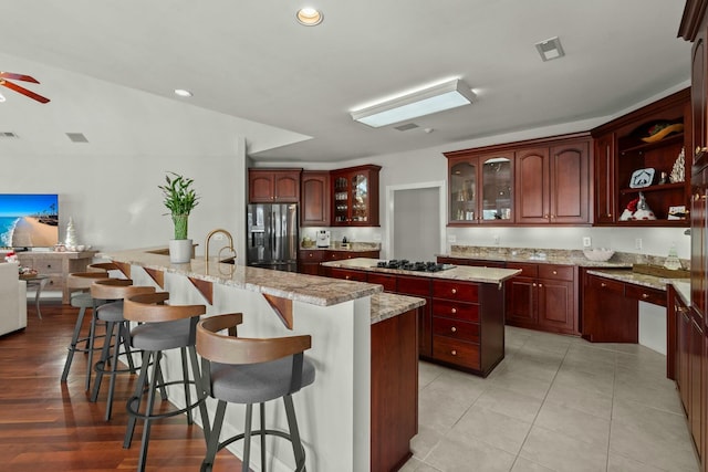 kitchen featuring a breakfast bar, a center island with sink, stainless steel fridge, light stone counters, and gas cooktop