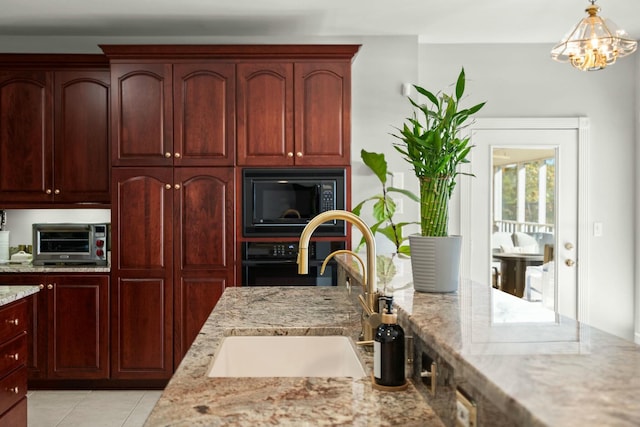 kitchen featuring pendant lighting, an inviting chandelier, black appliances, sink, and light stone countertops