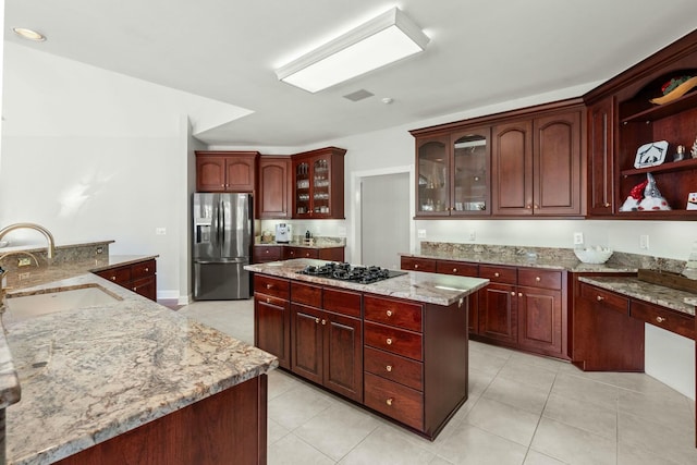 kitchen with a center island, black gas stovetop, sink, light stone countertops, and stainless steel fridge with ice dispenser