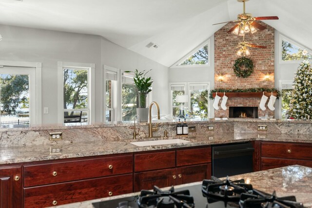 kitchen featuring a fireplace, light stone countertops, sink, and lofted ceiling