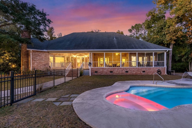 pool at dusk featuring a sunroom, a yard, and a patio