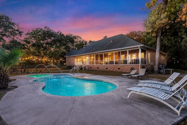 pool at dusk featuring a sunroom, a patio area, and pool water feature